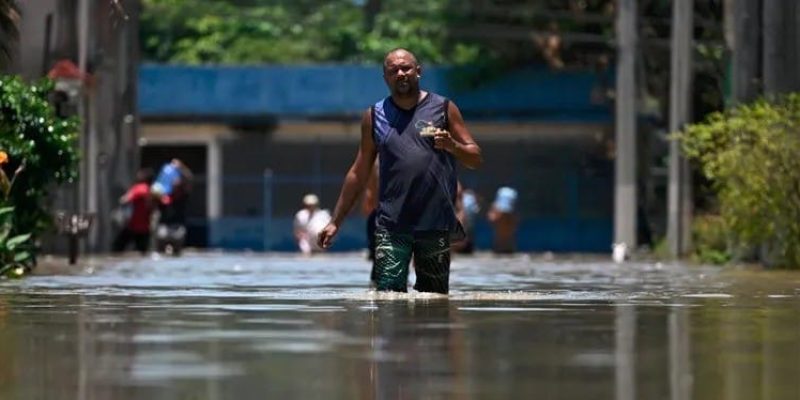 Homem caminha pela água em rua alagada na comunidade do Pilar, em Duque de Caxias (RJ) - Mauro Pimentel/AFP