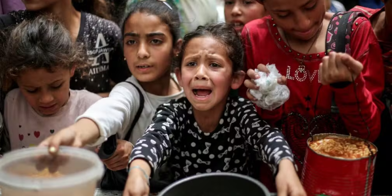 Menina chora enquanto aguarda que panela seja preenchida com alimento em Gaza — Foto: Eyad BABA / AFP