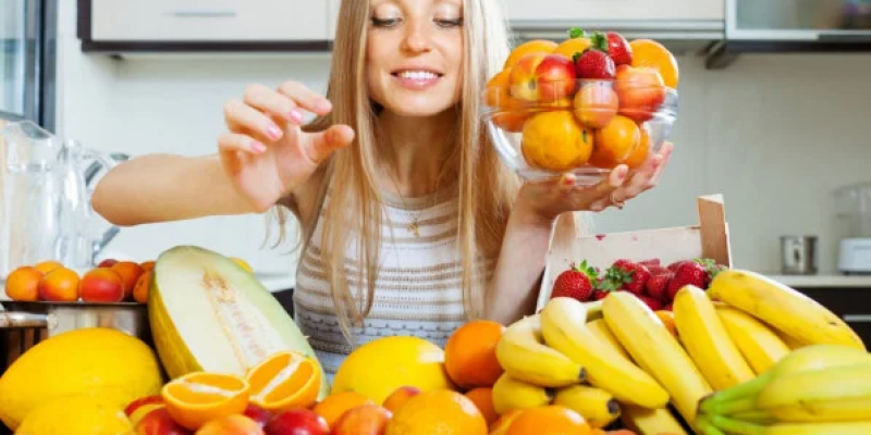 Mulher escolhendo frutas em uma mesa com grande variedade de opções - Reprodução/Freepik