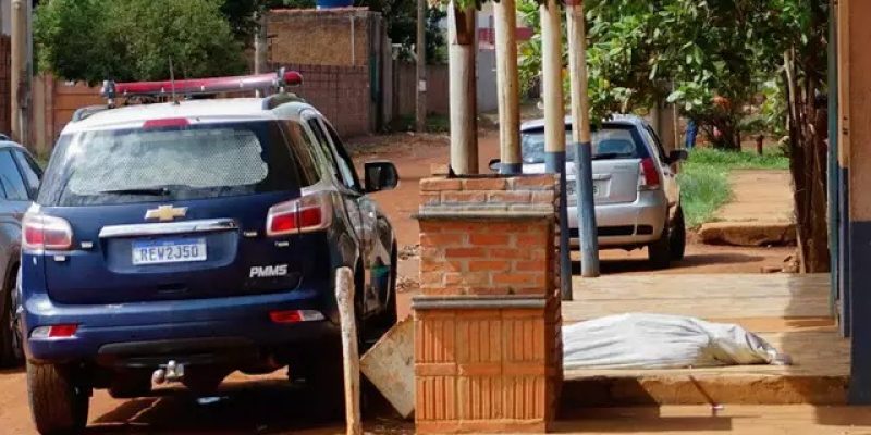 Corpo da vítima colocado em calçada ao lado de viatura da Polícia Militar (Foto: Alex Machado)