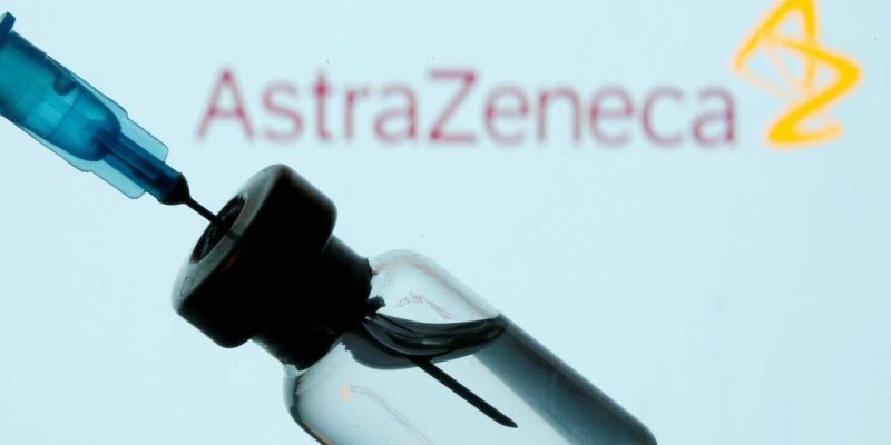 Frasco e seringa em frente ao logo da AstraZeneca em foto de ilustração